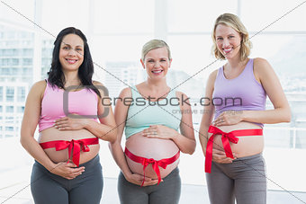 Happy pregnant women standing with red bow around bumps
