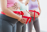 Pregnant women standing with red bow around bumps
