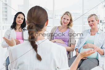 Pregnant women listening to gesturing doctor at antenatal class