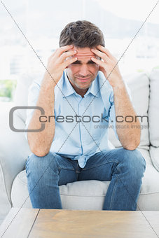 Handsome man sitting on the couch with headache looking at camera