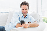 Happy man sitting on the couch sending a text