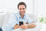 Smiling man sitting on the couch sending a text