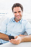 Cheerful man sitting on the couch sending a text