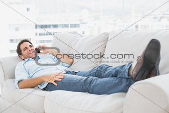 Happy man lying on the couch talking on the phone
