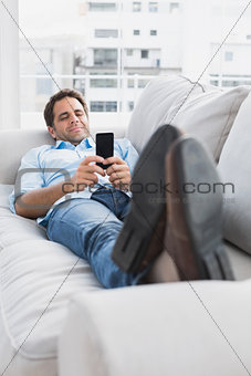 Happy man lying on the couch sending a text