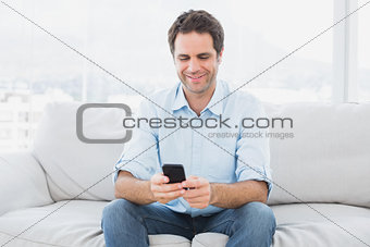 Happy man sitting on the couch sending a text message
