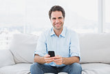 Cheerful man sitting on the couch sending a text message