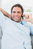 Happy man sitting on the couch on the phone smiling at camera