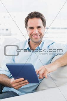 Handsome smiling man sitting on the sofa using his tablet pc