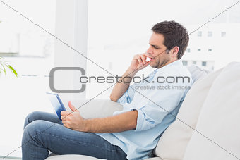 Serious man sitting on the couch using his tablet