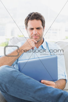 Thinking man sitting on the couch using his tablet