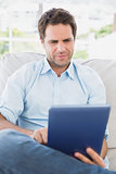 Focused man sitting on the couch using his tablet
