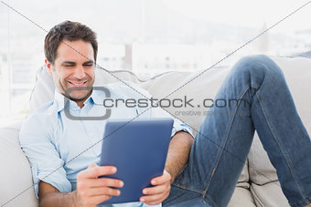 Smiling man relaxing on the couch using his tablet