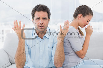 Man gesturing at camera with his crying partner on the couch