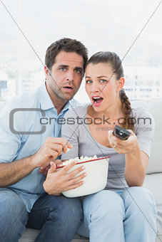Couple watching scary movie on the sofa with bowl of popcorn