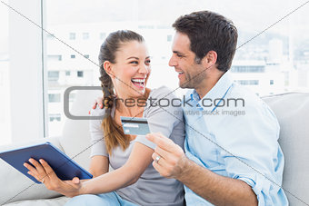 Laughing couple sitting on the couch shopping online with tablet pc