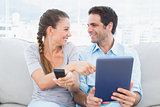 Smiling couple sitting on the couch using tablet pc and watching tv