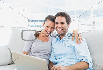 Happy couple sitting on the sofa using laptop together