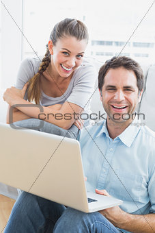 Happy couple using laptop smiling at camera