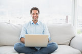 Happy man using laptop smiling at camera sitting on sofa