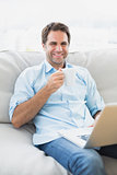 Happy man using laptop sitting on sofa having a coffee