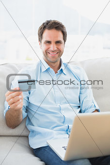 Smiling man using laptop sitting on sofa shopping online