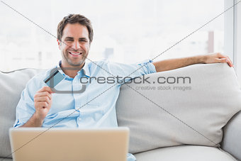 Happy man using laptop sitting on sofa shopping online