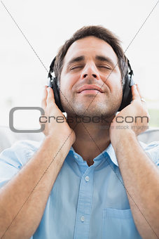 Content man sitting on sofa listening to music with eyes closed
