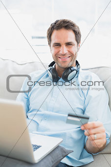 Smiling man sitting on sofa online shopping with laptop