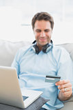 Smiling handsome man sitting on sofa online shopping with laptop