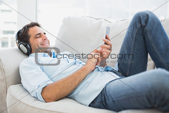 Happy handsome man lying on sofa using tablet and listening to music