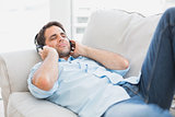 Happy handsome man lying on sofa listening to music
