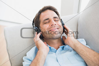 Smiling handsome man lying on sofa listening to music