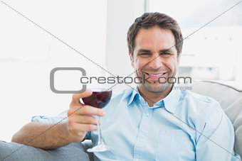 Happy man relaxing on sofa with glass of red wine