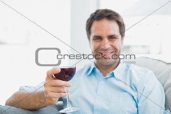 Cheerful man relaxing on sofa with glass of red wine
