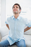 Handsome man sitting on sofa stretching painful back