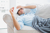 Sick man lying on sofa checking his temperature under a blanket
