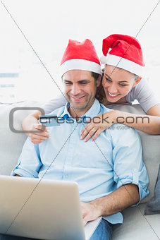 Cute couple in santa hats shopping online with laptop