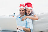 Smiling couple in santa hats shopping online with laptop