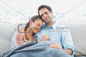 Cheerful couple relaxing on their sofa under blanket