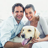 Happy couple petting their yellow labrador on the couch