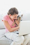 Happy woman holding her yorkshire terrier on the couch using laptop