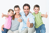 Cute family smiling at camera together showing thumbs up