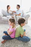 Siblings sitting back to back while parents are arguing