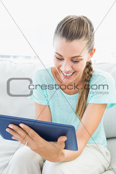 Happy woman sitting on couch using tablet pc