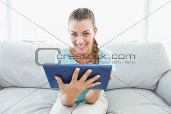 Cheerful woman sitting on couch using tablet pc