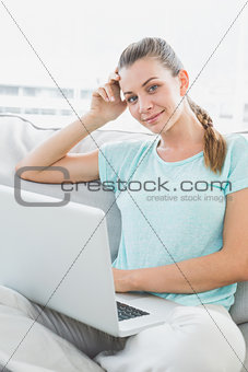 Smiling woman sitting on couch using her laptop