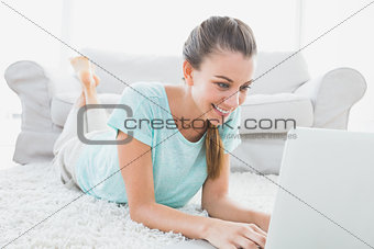 Happy woman lying on rug using her laptop