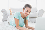 Smiling woman lying on rug using her laptop
