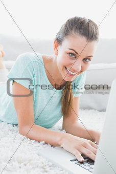 Cheerful woman lying on rug using her laptop